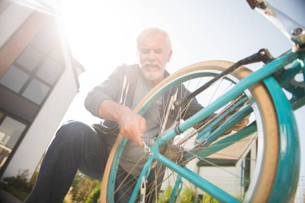 istock Bearded elderly man wearing dark jeans feeling busy repairing bicycle 1057952916