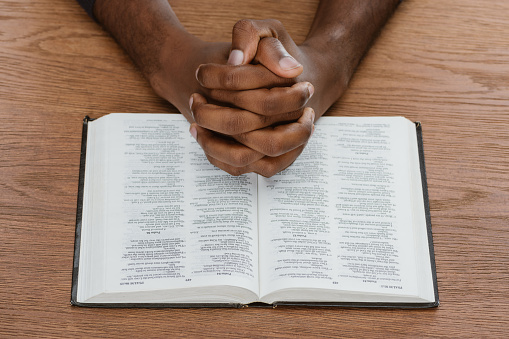 cropped shot of african american man praying with holy bible on wooden surface