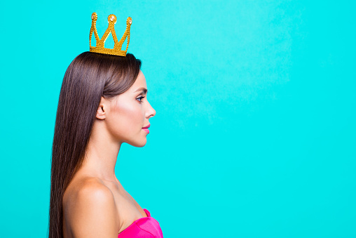 Half faced turned close up studio photo portrait of pretty attractive confident charming cute lovely serious lady wearing crown on head isolated on bright vivid blue background
