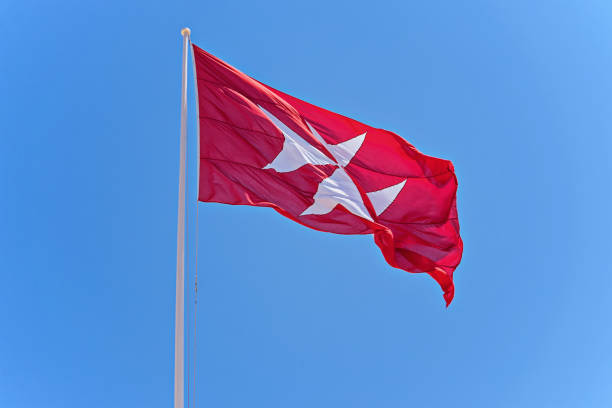 Red flag with black cross Red flag with black cross. Symbol of the Knights of Malta is the eight-pointed cross against blue sky, copy space, blowing waving in wind knights of malta stock pictures, royalty-free photos & images
