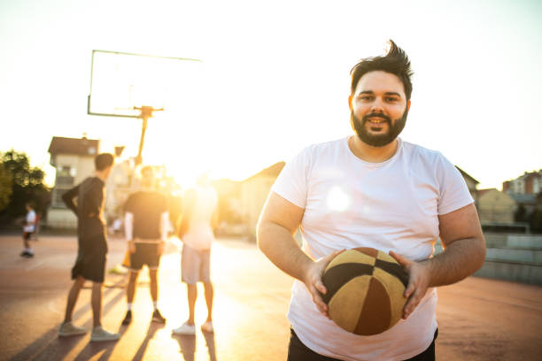 play-maker in sovrappeso essendo capitano della squadra di basket di oggi - streetball basketball sport men foto e immagini stock