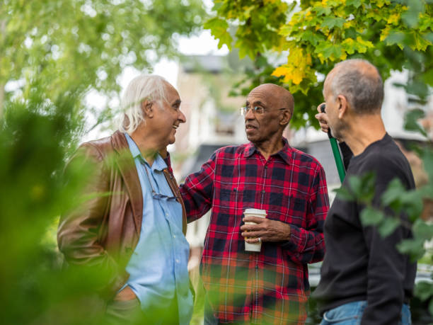 Senior neighbors friendly talk Group of senior men of various backgrounds having a friendly chat in the front yard of one man while he is raking the leafs. Bright fall scene on the road in the North American city. neighbour stock pictures, royalty-free photos & images