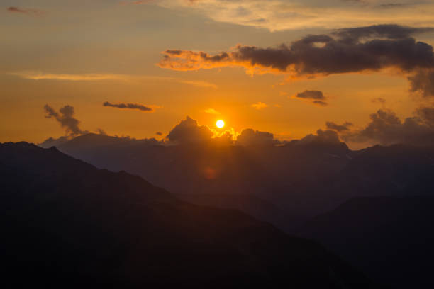 An orange sunset through the clouds above a range of mountains in the European alps.