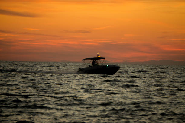 ein boot fährt zum strand bei sonnenuntergang - motorboat fishing cruise ship dawn stock-fotos und bilder