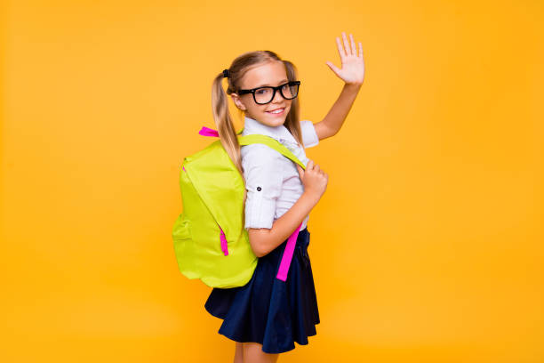 Photo of small girl turned around half a turn and waving hand look at camera isolated on bright yellow background with copy space for text Photo of small girl turned around half a turn and waving hand look at camera isolated on bright yellow background with copy space for text hello stock pictures, royalty-free photos & images