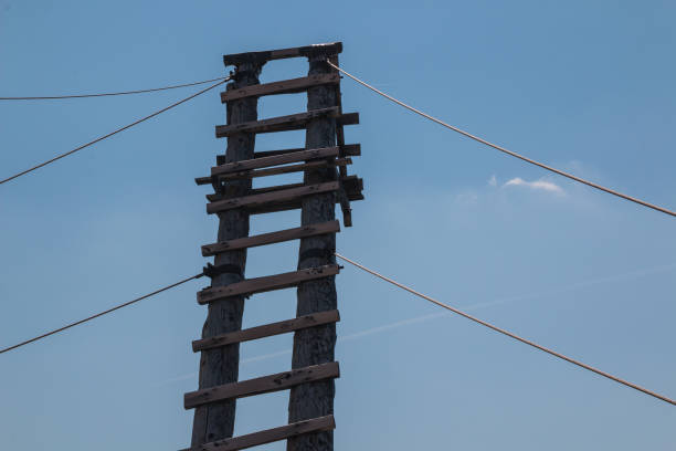 Ladder made of natural wood, tied to the ground with several ropes. Blue sky with a small cloud. Silo, island Krk, Croatia.