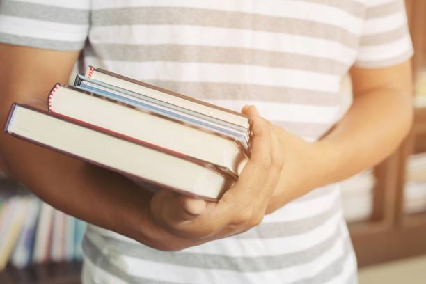 istock close up student young man hand holding books are placed front bookshelf in a library University. love to read education concept. with filter Tones retro vintage warm effect. 1058002744