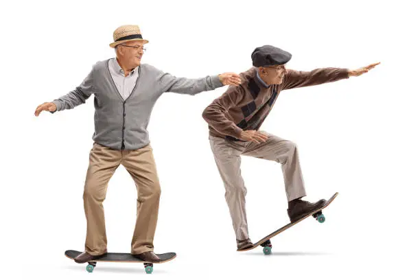 Full length profile shot of two elderly men skateboarding isolated on white background