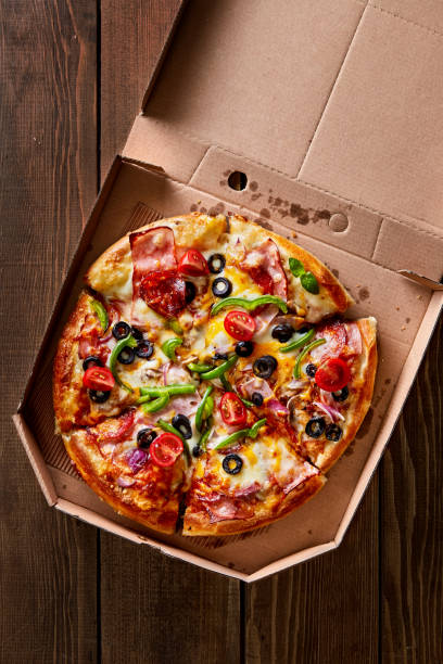 istock Pizza in a cardboard box on a wooden table viewed from above. Pizza delivery concept. Top view 1058005366