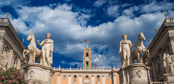 Capitoline Hill with ancient roman statues and renaissance clocktower with clouds, in the very center of Rome