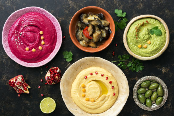 istock Colorful hummus in bowls on a dark rustic background, traditional hummus, hummus with basil, beet hummus. Top view, flat lay. Clean eating, dieting, vegetarian party food 1058032192