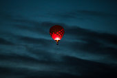 Colorful hot air balloon in dark pink and purple colors glowing in a dark blue early morning sky