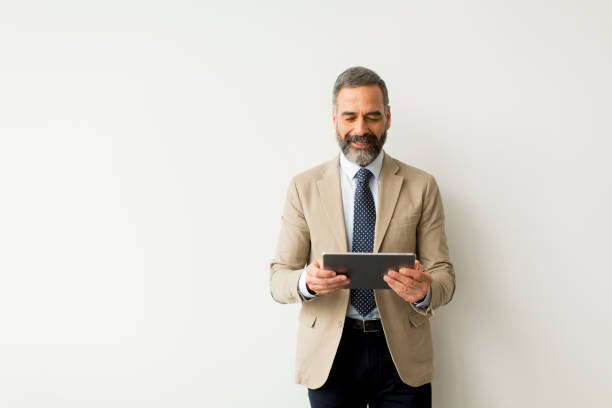 istock Handsome senior businessman with digital tablet by wall 1058044120
