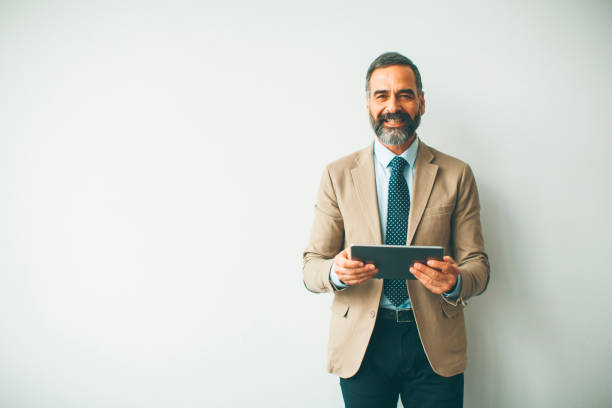 istock Handsome senior businessman with digital tablet by wall 1058044124