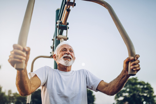 Senior bearded man exercising in a outdoor gym, living the healthy lifestyle.