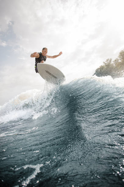 Active man jumping on the white wakeboard on the wave Active man jumping on the white wakeboard on the wave having healthy summertime on the river on the background of sky jump board stock pictures, royalty-free photos & images