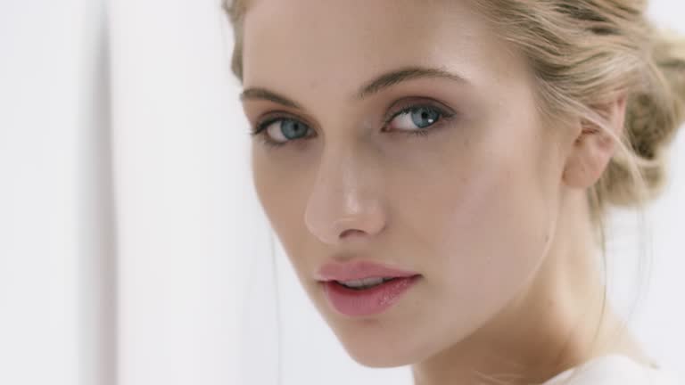 Close-up portrait of young woman with attractive blue eyes. Zoom in shot of beautiful female. She is by wall against white background.