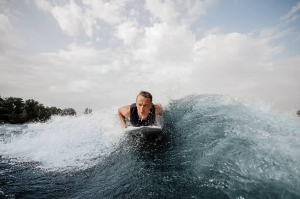 istock Young active man lying on the white wakeboard on the blue wave 1058045628