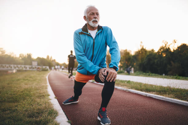 uomo anziano che si allunga mentre fa jogging su una pista da corsa - streatching foto e immagini stock