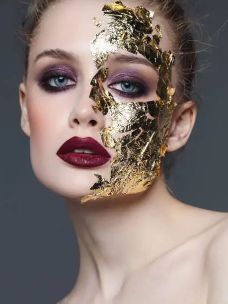 Studio portrait of beautiful woman with bright make-up and golden foil