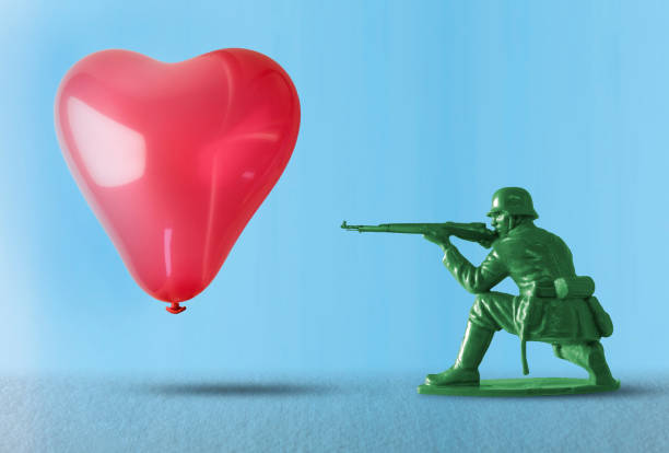 Heart balloon as a target for a soldier holding a gun Toy soldier pointing a gun at heart shaped balloon floating as a target - representing the negative impact of war and the destruction of the flow of love with gun crime end gun violence stock pictures, royalty-free photos & images