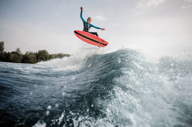 istock Active boy dressed in black and blue swimsuit wakesurfing jumping up on orange board 1058060394