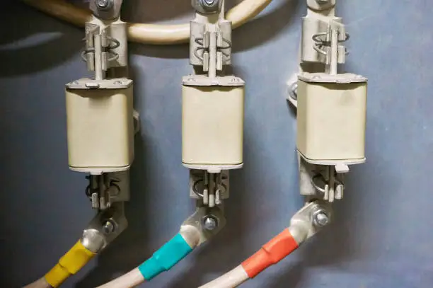 Photo of Three electrical high-voltage fuses connected to the colored wires. Industrial background.
