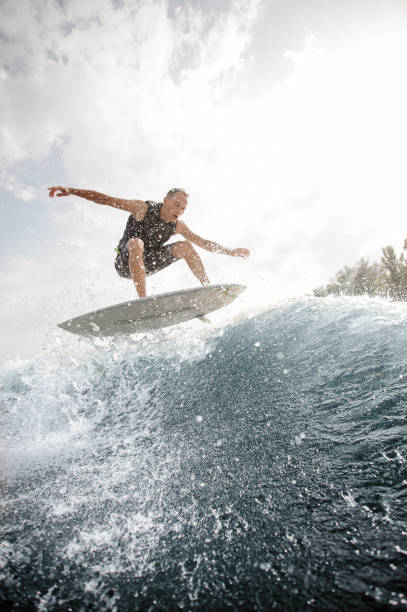 istock Young man jumping on the white wakeboard down the blue water against grey sky 1058061562