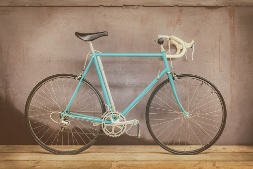Vintage seventies light blue racing bicycle on a wooden floor with a weathered background wall