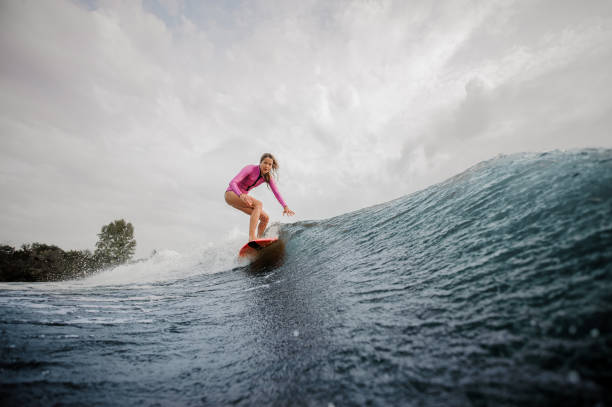 istock Active woman wakesurfer riding down the blue splashing wave against sky 1058061768