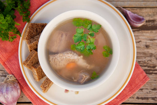 istock Clear beef broth, bouillon in white bowl and vegetables on wooden table. Rustic style. Top view. 1058068914