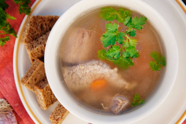 istock Clear beef broth, bouillon in white bowl and vegetables on wooden table. Rustic style. Top view. 1058068940