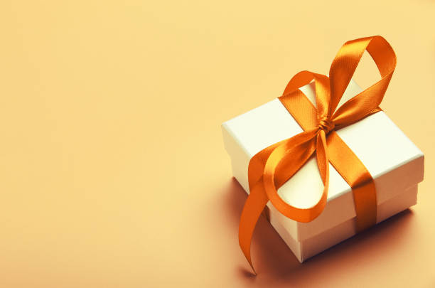 White gift box with orange bright ribbon on yellow background. Beautiful gift for the new year, Christmas, birthday. Copy space White gift box with orange bright ribbon on yellow background. Beautiful gift for the new year, Christmas, birthday. Copy space. anniversary gifts stock pictures, royalty-free photos & images