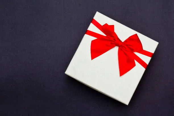 White gift box with red ribbon on black background. Top view.