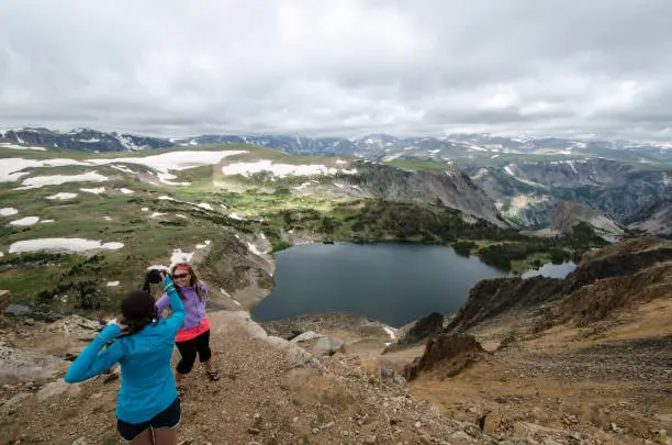 Two female friends (20s) take pictures of each other at an overlook along Montana Beartooth Pass Highway in the Rocky Mountains