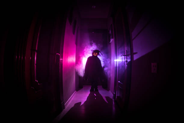 istock Halloween concept. Creepy silhouette in the dark corridor with pumpkin head. Toned light with fog on background. Selective focus 1058099764