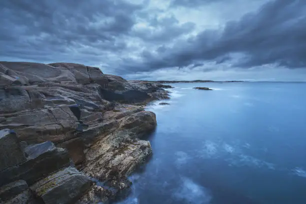 A wide angle view of ominous clouds over a rugged rocky coastline.