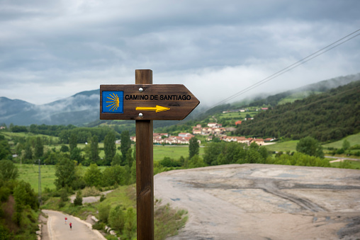 Sign for the Camino de Santiago near Zubiri, Navarra, Spain. Two hikers are visible walking the Camino in the lower left of the image.
