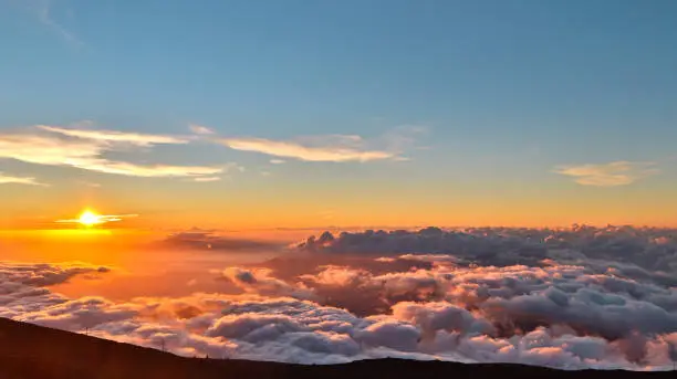 Orange sunset above the clouds on the top of Haleakala volcano, Maui, Hawaii