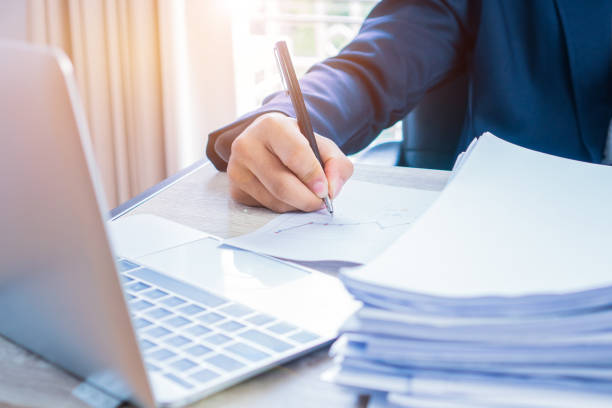 istock Businessman hands working and writing data in computer, Stacks of paper files for searching information on work office, business report papers,piles of unfinished documents achieves with clips indoor 1058161466
