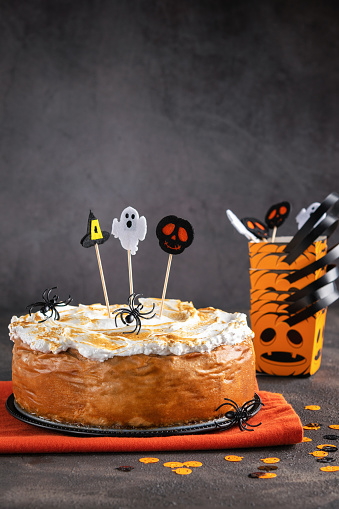 Halloween Party Pumpkin Cheesecake with Marshmallow Meringue Topping decorated with Halloween toppers. Dessert for Halloween and Thanksgiving Background. Space for text. Vertical. Selective focus.