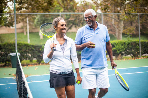coppia nera senior che gioca a doppio tennis - senior adult senior couple exercising african ethnicity foto e immagini stock