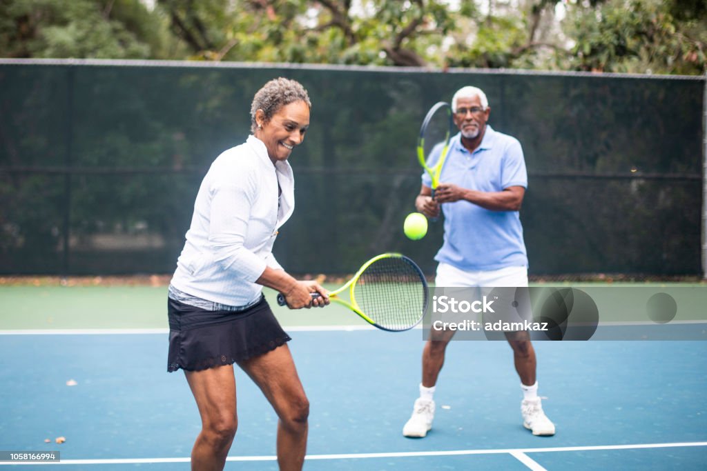 Senior Black Couple Playing Doubles Tennis A Senior Black Couple Playing Doubles Tennis on a cloudy morning Tennis Stock Photo