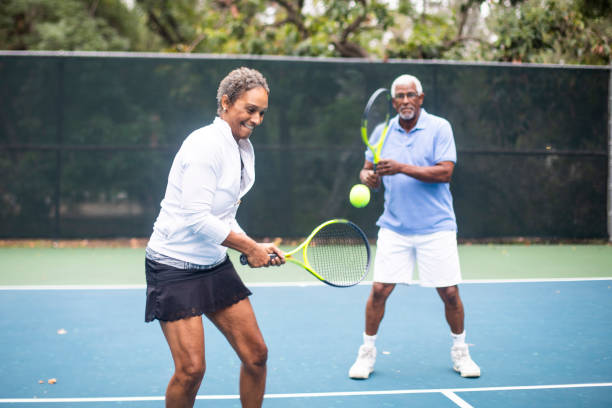 senior black couple playing doubles tennis - tennis active seniors healthy lifestyle senior men imagens e fotografias de stock