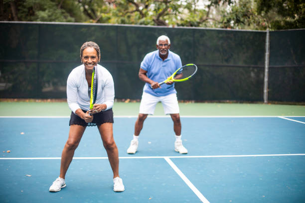 senior black couple playing doubles tennis - tennis couple women men imagens e fotografias de stock