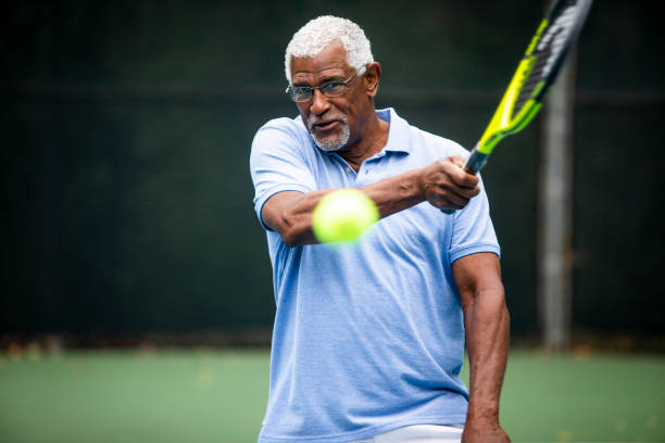 senior schwarzer mann spielen tennis - senior adult healthy lifestyle athleticism lifestyles stock-fotos und bilder