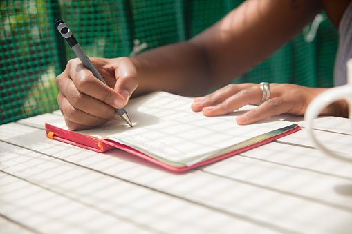 Close up of unrecognizable black woman writing on her notebook while sitting on porch