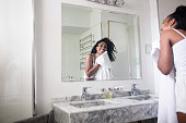 Beautiful black woman drying her face with a towel while looking at herself in the mirror smiling