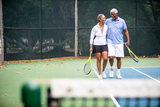 coppia nera senior sul campo da tennis - senior adult senior couple exercising african ethnicity foto e immagini stock