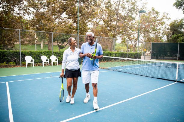 älteres schwarzes paar zu fuß neben dem tennisplatz - tennis active seniors healthy lifestyle senior men stock-fotos und bilder